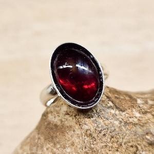 May include: A silver ring with a dark red oval gemstone set in a silver bezel.