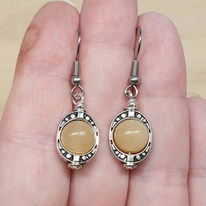 May include: A pair of silver dangle earrings with a light brown round stone set in a decorative silver frame.
