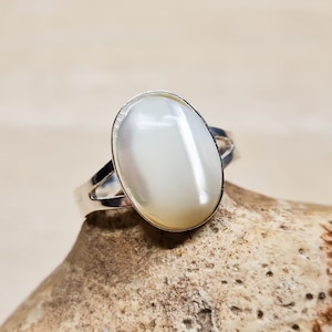 May include: A silver ring with a white oval-shaped mother of pearl stone.