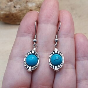 May include: A pair of silver dangle earrings with turquoise stones set in a decorative oval frame.