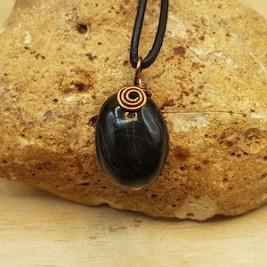 May include: Black gemstone pendant with a copper wire wrap, hanging from a black cord.
