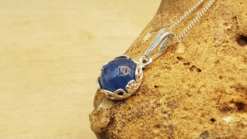 May include: A silver pendant necklace with a blue gemstone set in a silver filigree design.