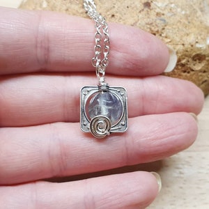 May include: A silver necklace with a square pendant featuring a clear crystal encased in wire. The pendant has a delicate silver chain.