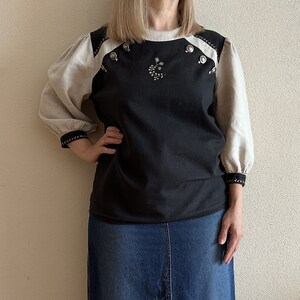 May include: A black and white blouse with a floral design and silver buttons. The blouse has a round neckline and long sleeves with a white trim.