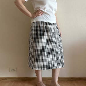 Op de afbeelding: Een wit T-shirt gecombineerd met een zwart-wit geblokte midi-rok.