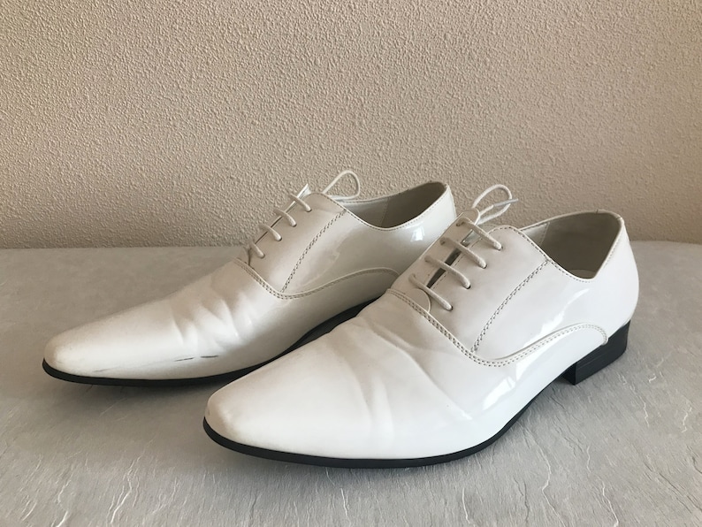 May include: Two pairs of white leather dress shoes with lace-up fastenings.