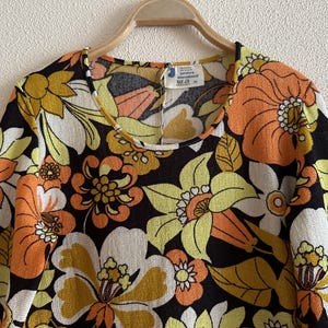 May include: A black long-sleeved dress with a large floral print in shades of orange, yellow, and white. The dress has a round neckline and a loose fit.