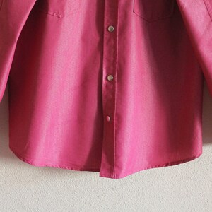 May include: A long-sleeved, pink button-down shirt with a single chest pocket.