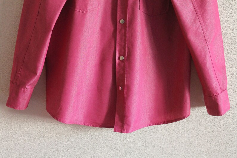 May include: A long-sleeved, pink button-down shirt with a single chest pocket.