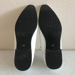 May include: A pair of white leather shoes with black soles. The shoes have a pointed toe and a size 40 label on the sole.