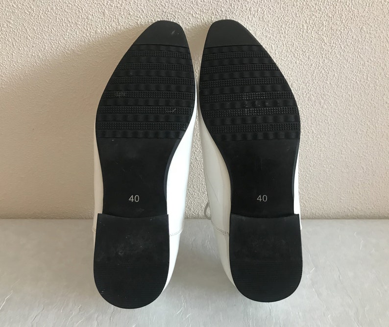 May include: A pair of white leather shoes with black soles. The shoes have a pointed toe and a size 40 label on the sole.