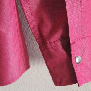 May include: A close-up of a burgundy long-sleeved shirt with a single button on the cuff.