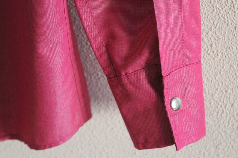 May include: A close-up of a burgundy long-sleeved shirt with a single button on the cuff.