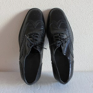 May include: A pair of black leather brogue shoes with lace-up closures. The shoes have a wingtip design and a polished finish.