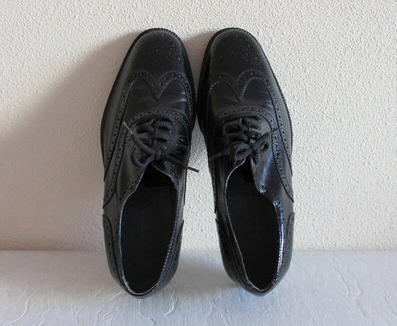 May include: A pair of black leather brogue shoes with lace-up closures. The shoes have a wingtip design and a polished finish.