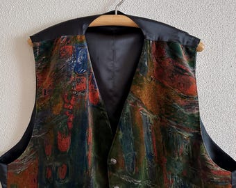 May include: A colorful vest with a unique abstract design in shades of red, green, blue, and brown. The vest has a black satin collar and lining, and is hanging on a wooden hanger.