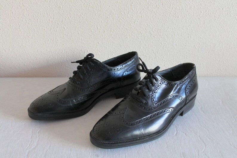 May include: A pair of black leather lace-up shoes with wingtip detailing. The shoes have a classic brogue design and a polished finish.