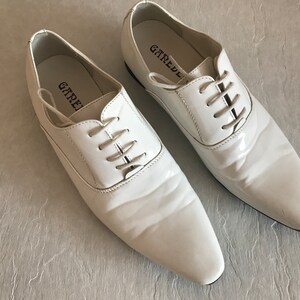 May include: A pair of white leather lace-up shoes with a pointed toe. The shoes have the brand name "GAREDE" printed on the inside of each shoe.