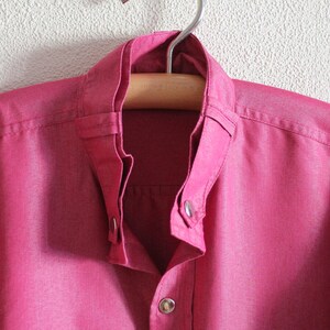 May include: A pink button-down shirt with a mandarin collar and a single button closure at the neck.