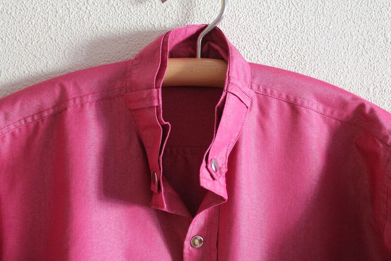 May include: A pink button-down shirt with a mandarin collar and a single button closure at the neck.