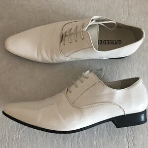 May include: A pair of white leather lace-up shoes with a pointed toe and black soles. The brand name "GARREDE" is printed on the side of the right shoe.