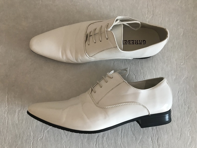 May include: A pair of white leather lace-up shoes with a pointed toe and black soles. The brand name "GARREDE" is printed on the side of the right shoe.