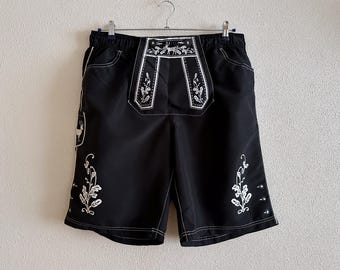 May include: Black swim trunks with white embroidered floral designs and a deer motif. The waistband has a white elastic band.