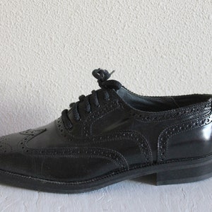 May include: Black leather oxford shoes with a wingtip design and lace-up closure.