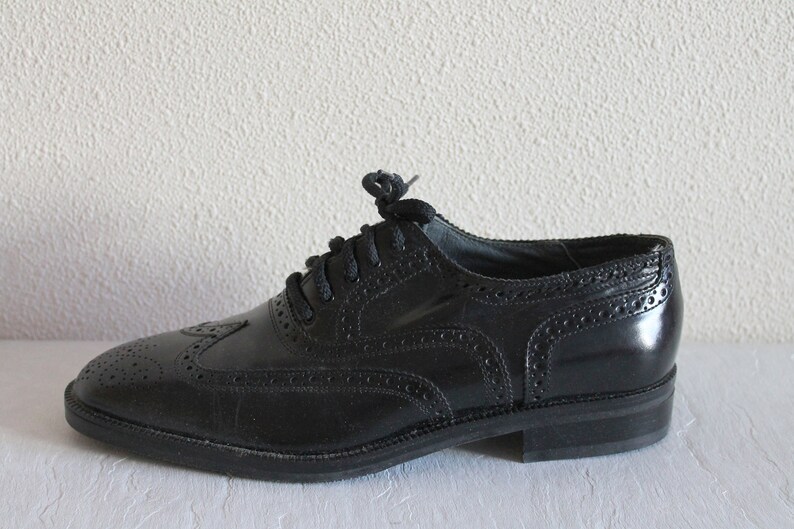 May include: Black leather oxford shoes with a wingtip design and lace-up closure.