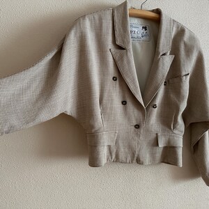 May include: A brown and white checkered blazer with a double-breasted closure and long sleeves. The blazer has a cropped length and a relaxed fit.
