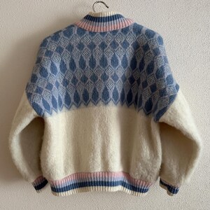 May include: A vintage-style sweater with a high collar, featuring a color-blocked design. The upper portion is light blue with a diamond pattern, while the lower half is off-white. The collar and cuffs have pink and blue stripes.