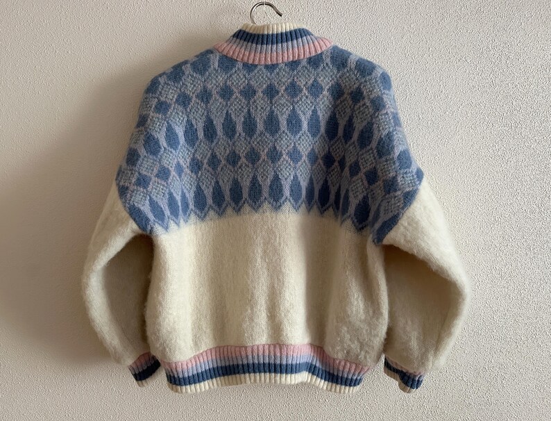 May include: A vintage-style sweater with a high collar, featuring a color-blocked design. The upper portion is light blue with a diamond pattern, while the lower half is off-white. The collar and cuffs have pink and blue stripes.