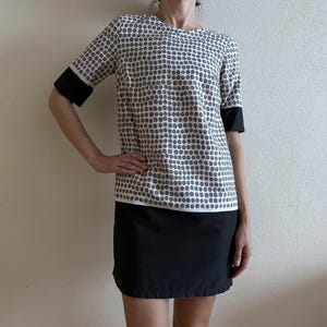 May include: A two-piece outfit comprising a short-sleeved top and a skirt. The top has a white base with a pattern of grey dots, black cuffs, and a black skirt. The outfit is a simple, yet stylish design.