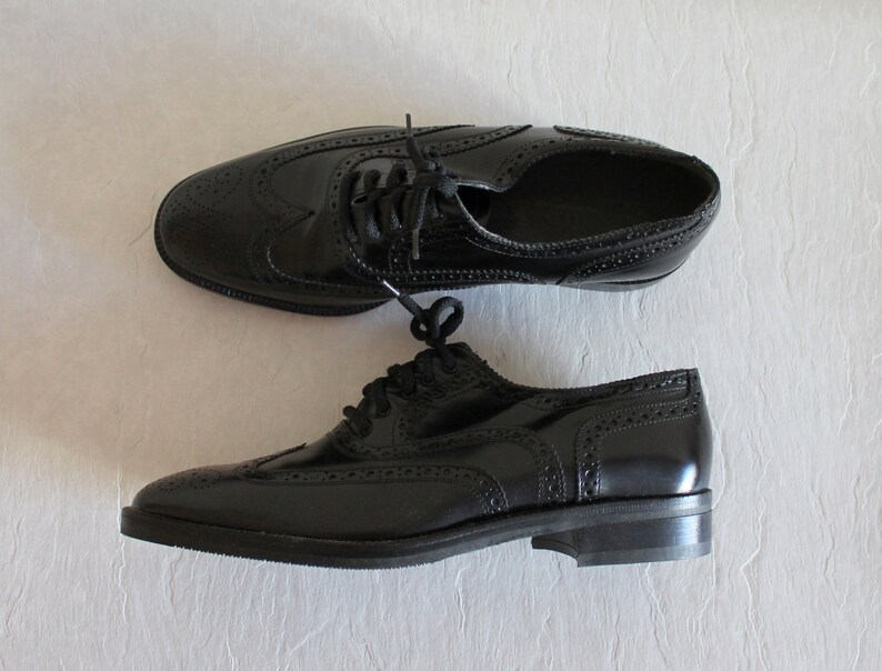 May include: A pair of black leather oxford shoes with brogue detailing. The shoes have a lace-up closure and a rounded toe.