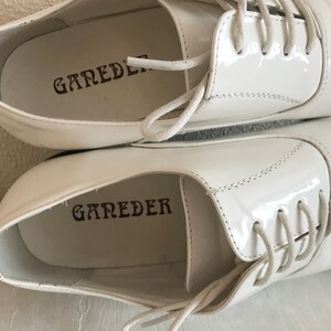 May include: A pair of white leather shoes with white laces. The shoes have the word "GAREDER" printed on the inside of each shoe.