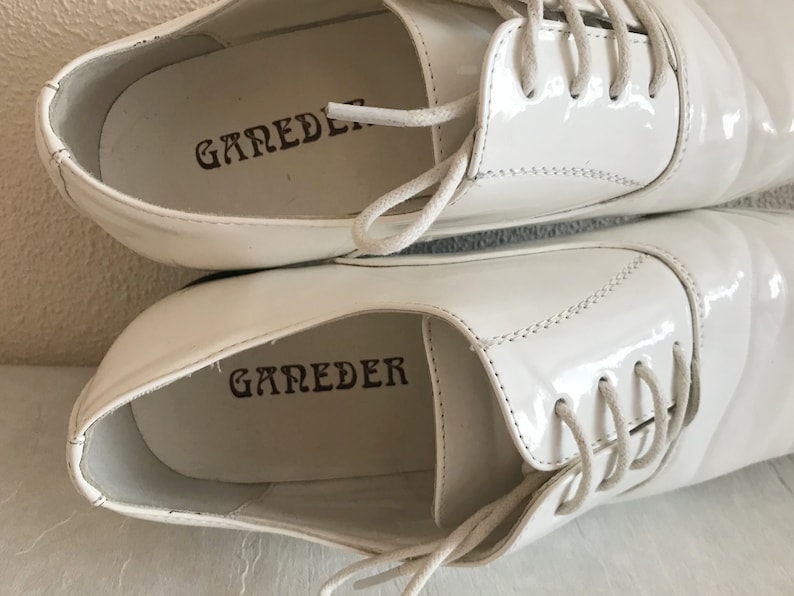 May include: A pair of white leather shoes with white laces. The shoes have the word "GAREDER" printed on the inside of each shoe.