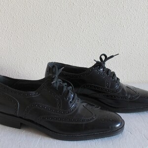 May include: A pair of black leather oxford shoes with brogue detailing and lace-up closures.