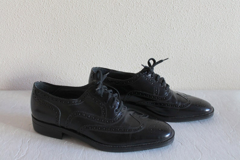 May include: A pair of black leather oxford shoes with brogue detailing and lace-up closures.