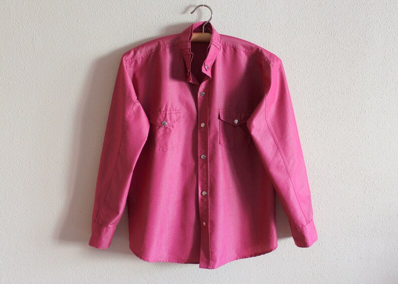 May include: A long-sleeved, pink button-down shirt with two chest pockets and a pointed collar.