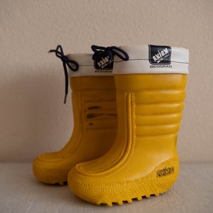 May include: A pair of yellow rubber boots with white and blue trim. The boots have a textured sole and the brand name "Akim" is printed on the side.