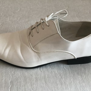 May include: A pair of white leather lace-up shoes with a pointed toe and a black rubber sole.