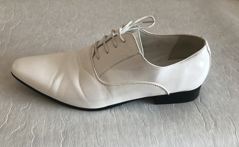 May include: A pair of white leather lace-up shoes with a pointed toe and a black rubber sole.