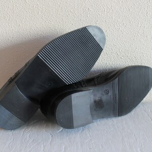 May include: A pair of black leather shoes with a brogue design. The shoes have a rubber sole with a textured pattern.