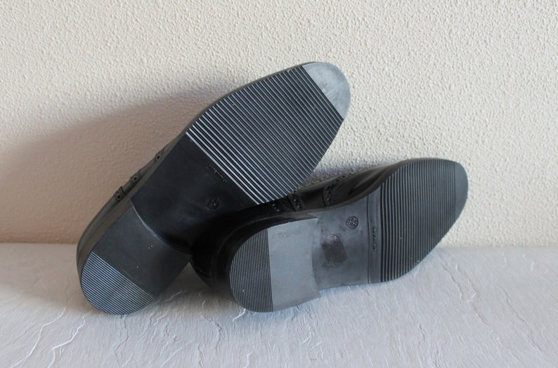 May include: A pair of black leather shoes with a brogue design. The shoes have a rubber sole with a textured pattern.