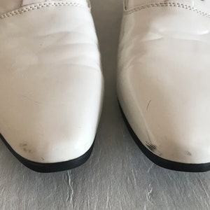 May include: A pair of white leather dress shoes with black trim. The shoes have a pointed toe and a lace-up closure.