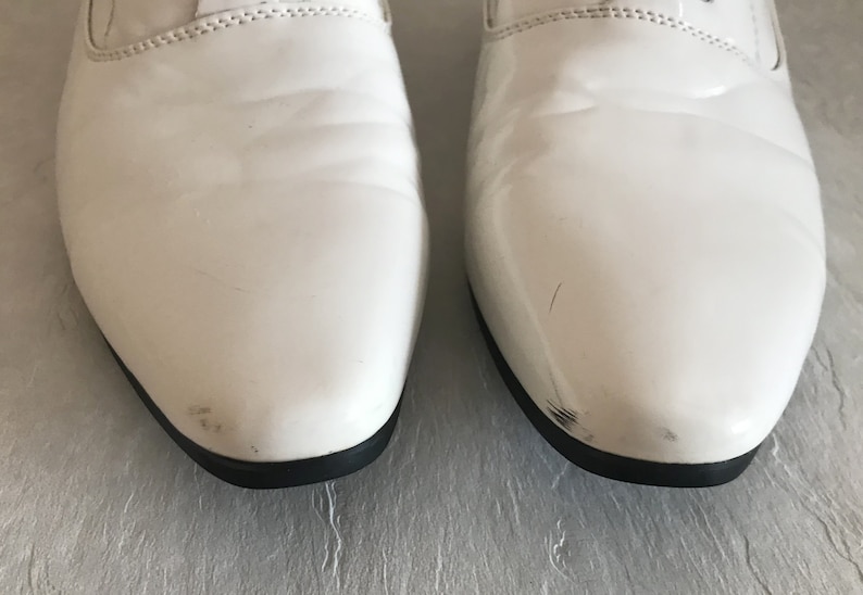 May include: A pair of white leather dress shoes with black trim. The shoes have a pointed toe and a lace-up closure.