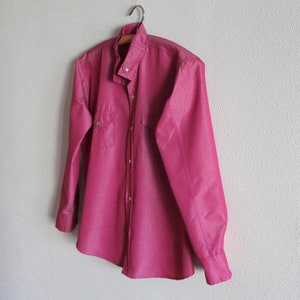 May include: A long-sleeved, button-down shirt in a deep pink color. The shirt has a mandarin collar and a single chest pocket.