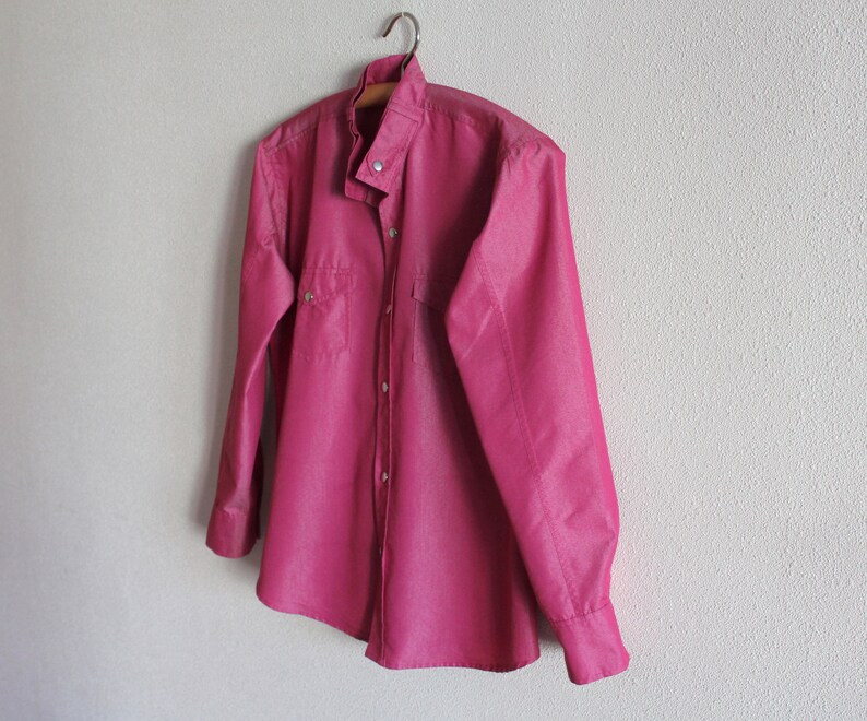 May include: A long-sleeved, button-down shirt in a deep pink color. The shirt has a mandarin collar and a single chest pocket.