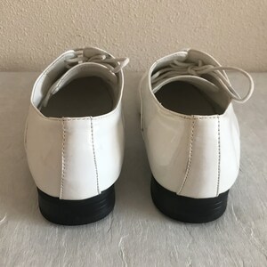 May include: A pair of white patent leather lace-up shoes with black soles.