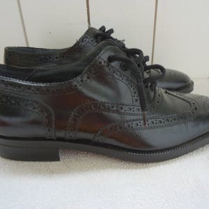 May include: A pair of black leather brogue shoes with lace-up closures. The shoes have a wingtip design and a polished finish.